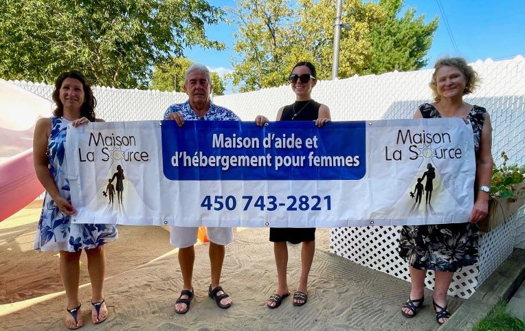 Photo de 4 personnes affichant une bannière pour la Maison La Source qui vient en aide aux femmes victimes de violences conjugales