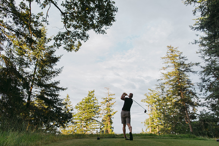 Un homme frappe une balle sur un terrain de golf boisé.