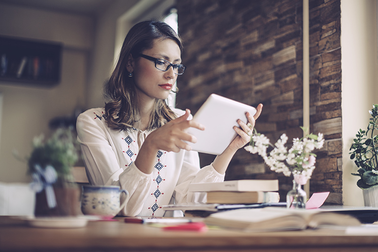 Serene woman is reading her digital tablet. She is sitting at the desk. Candid shoot.