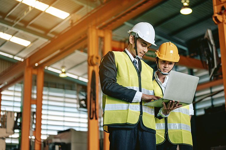 Collègues qui discutent devant un ordinateur d'assurance en matière de protection en portant un veston jaune de construction et u n casque de protection.