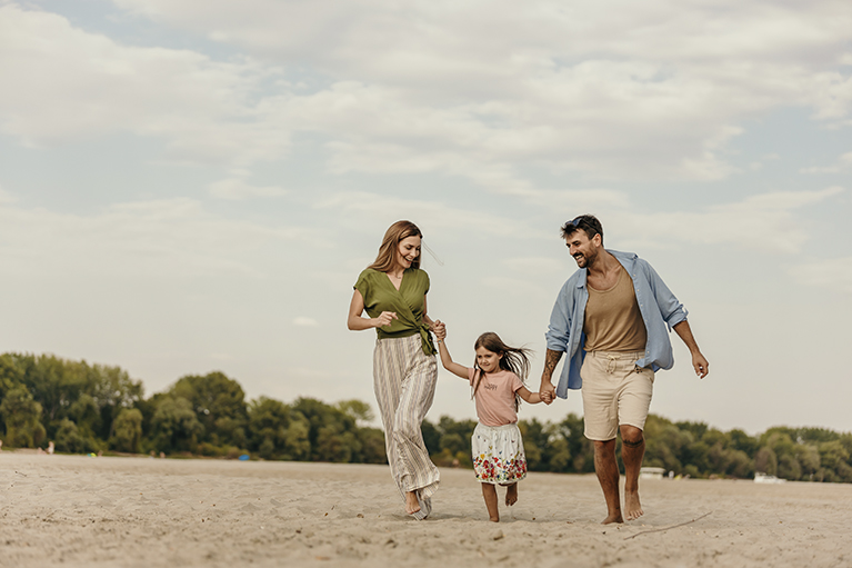 Mère, père et leur jeune fille qui courent, main dans la main, à la plage.