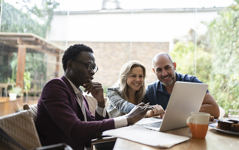 Image d'un couple regardant l'écran de l'ordinateur de leur conseiller en gestion de patrimoine. 