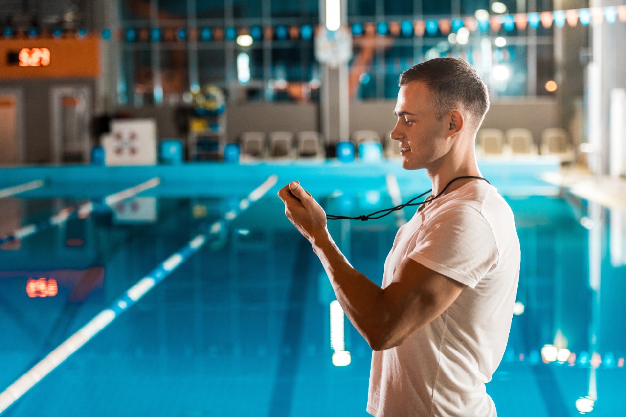 Un homme qui chronomètre des nageurs dans une piscine.