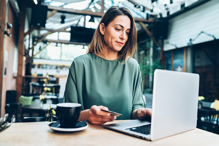 Young woman shopping online in cafe using lap top and credit card