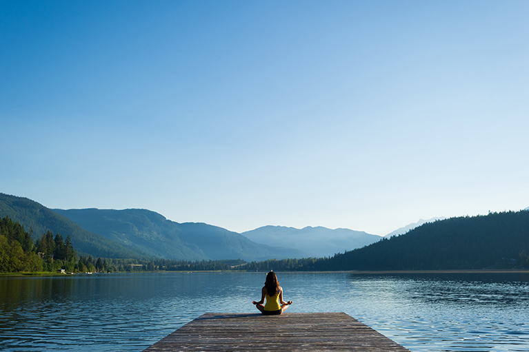 Femme assise sur un ponton face à un lac bleu.
