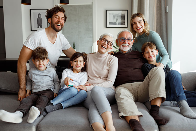 Trois enfant et quatre adultes sur un divan gris souriant.