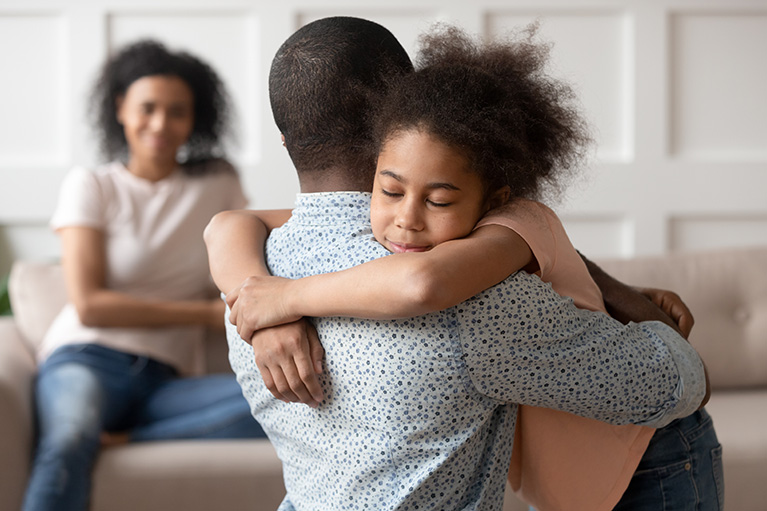 Une fille fessant un câlin à son père pendant que sa mère regarde.