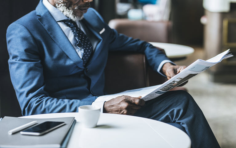 homme d'affaires noir assis dans un café qui lie un journal sur l'actualité financière