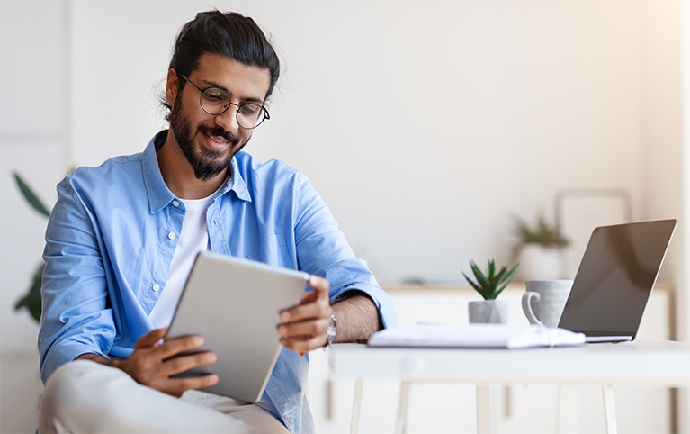 Un homme assis à un bureau, lisant quelque chose sur sa tablette.