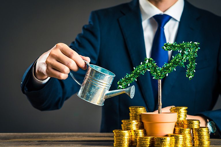 Une plante entourée par des pièces d'or devant une personne en veston tenant un arrosoir.