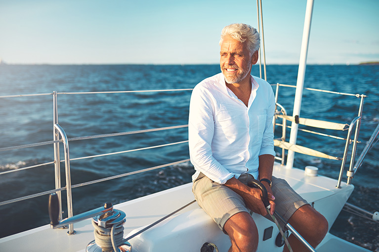 Homme d'une cinquantaine d'année assis souriant et heureux sur un bateau.
