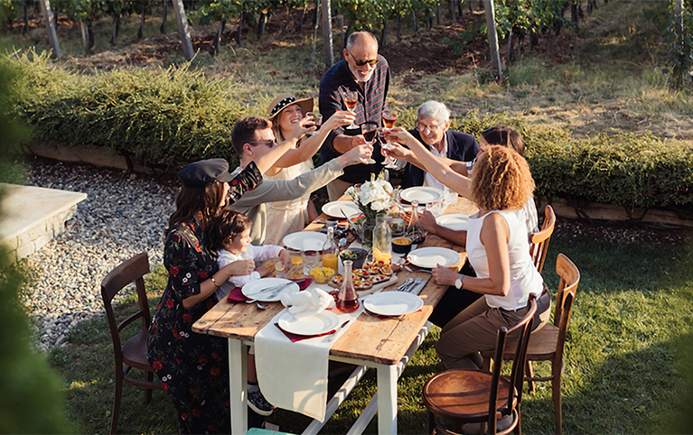 Une famille qui trinquent autour d’une table dans une cour.