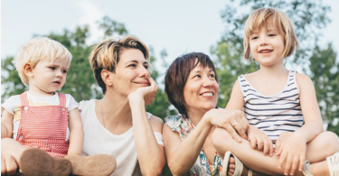 Une famille composée de deux mamans d'une quarantaine d'années et de deux enfants en bas âge sont face à l'objectif. Les deux mamans regardent leurs enfants avec bienveillance et en souriant.