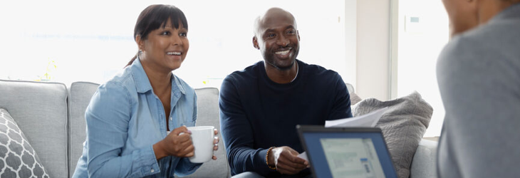 Couple souriant à son domicile en train de discuter avec son conseiller en gestion de patrimoine