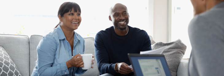 Couple souriant à son domicile en train de discuter avec son conseiller en placement