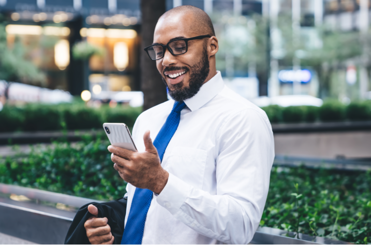 Un jeune conseiller, en chemise et cravate, consultant l'hebdo économique depuis son téléphone intelligent, souriant