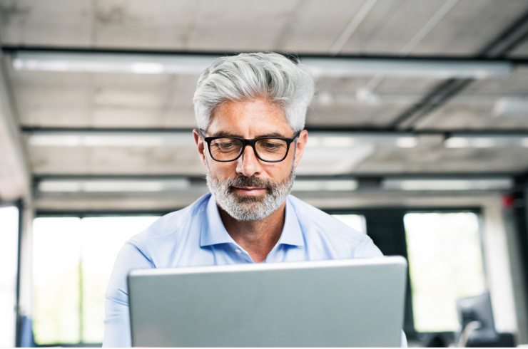 Un homme, cheveux grisonnants et lunettes, face à son ordinateur portable
